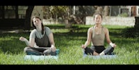 two women meditating in the grass