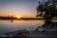 the sun is setting over a river near a dock