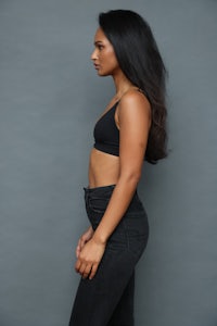 a woman in a black top and black pants is posing on a gray background