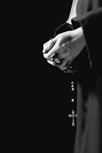 a black and white photo of a priest holding a rosary