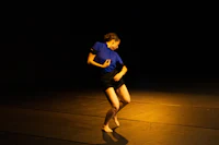 a woman in a blue shirt is dancing on a dark floor