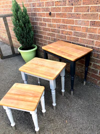 three wooden tables with potted plants in front of a brick wall