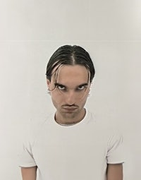 a man in a white t - shirt is standing in front of a white wall