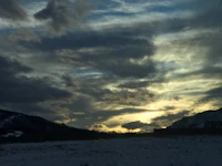the sun is setting over a snowy field with mountains in the background