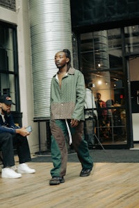 a man in a green jacket walking on a wooden floor