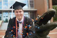 a man in a graduation cap and gown sitting next to a crocodile