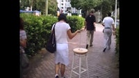 a group of people walking down a sidewalk with a stool