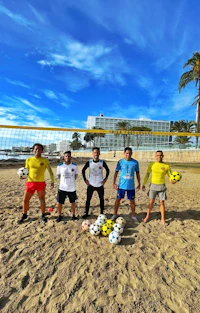 a group of men posing with soccer balls on the beach