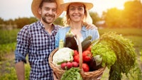 a couple holding a basket of vegetables in a field