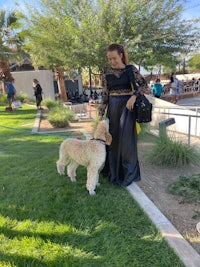 a woman in a black dress standing next to a poodle