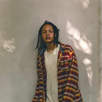 a young man with dreadlocks leaning against a wall