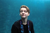 a young woman in a blue shirt standing in front of an aquarium