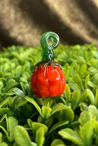 a small glass pumpkin sitting on top of green leaves