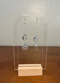 a pair of silver dangling earrings on a wooden stand