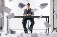 a businessman sitting at a table with papers flying around him