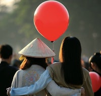 two women holding a red balloon in front of a crowd