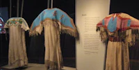 four native american dresses on display in a museum