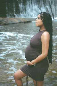 a pregnant woman standing in front of a waterfall