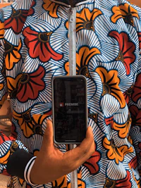 a person holding up a cell phone in an african print jacket