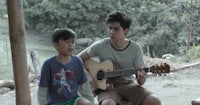 a boy and a girl sitting on a wooden bench playing acoustic guitar
