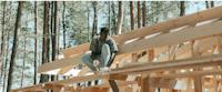 a man sitting on the roof of a house in the woods