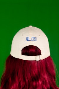 the back of a woman with red hair wearing a hat that says all cru
