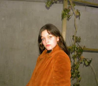 a woman in a brown coat standing in front of a wall