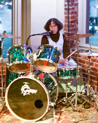 a person playing drums in front of a brick wall