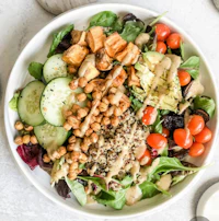 a bowl of salad with chickpeas, tomatoes and dressing