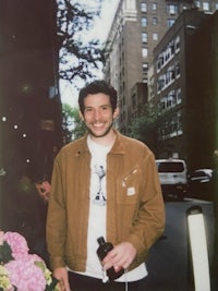 a man in a brown jacket smiling in front of flowers