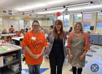 three women in orange aprons standing in a classroom