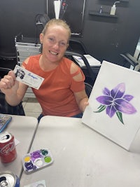 a woman holding up a painting of a purple flower