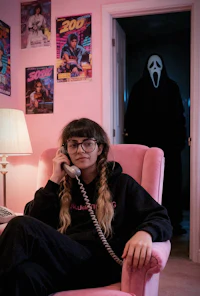 a woman talking on the phone in a pink chair next to a scream mask
