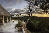 a house with a thatched roof overlooking the jungle at sunset