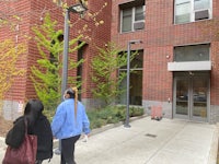 two women walking down the sidewalk in front of an apartment building