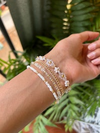 a woman's hand is holding a bracelet with pearls and crystals
