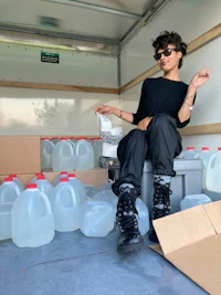 a woman sitting in the back of a truck full of water jugs