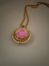 a gold necklace with a pink flower on it