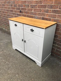 a white sideboard with wooden drawers in front of a brick wall