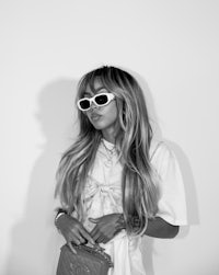 a black and white photo of a woman wearing sunglasses and a purse