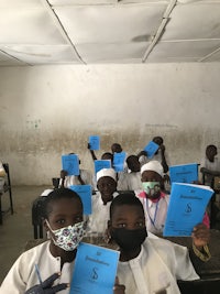 a group of children holding blue books in a classroom