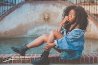 a young black woman in a denim jacket sitting on a fountain