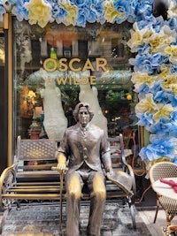 a statue of oscar wilde sits on a bench in front of a store