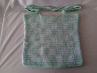 a green and white crocheted bag on a bed