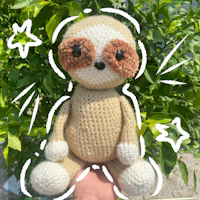 a crocheted sloth sitting in someone's hand