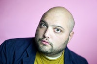 a bald man with a jacket and a yellow shirt