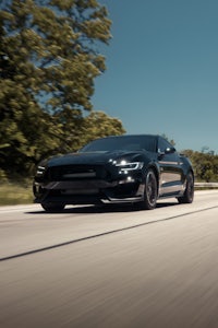 a black ford mustang is driving down a road