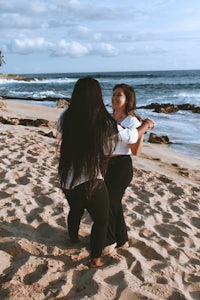 two women dancing on the beach in front of the ocean