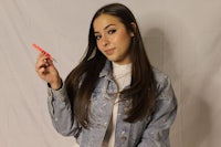 a girl in a denim jacket holding a pink lipstick