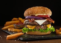 a burger with bacon, cheese and fries on a slate